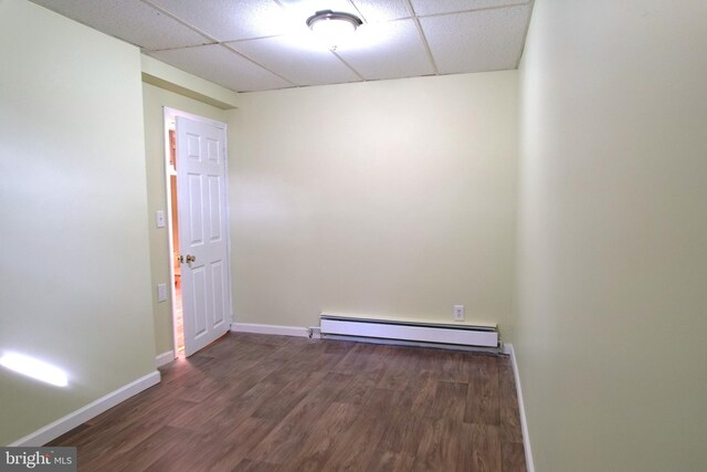 empty room featuring a baseboard heating unit, a drop ceiling, and dark hardwood / wood-style floors