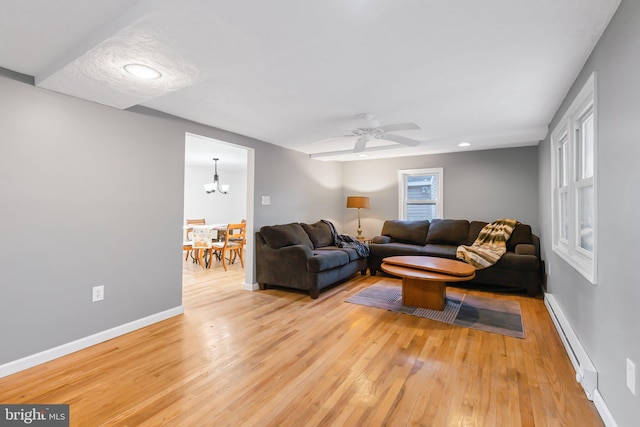 living room featuring baseboard heating, light wood-type flooring, and ceiling fan with notable chandelier