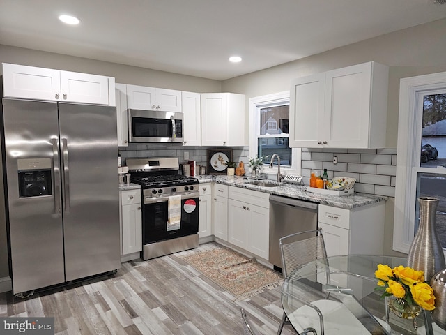 kitchen with sink, light stone counters, stainless steel appliances, and white cabinetry