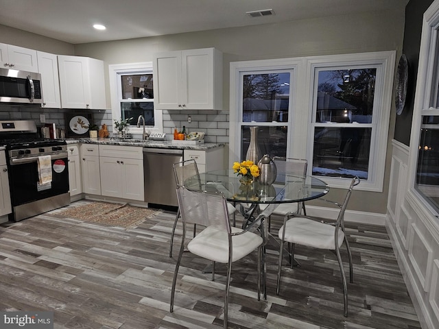 kitchen with appliances with stainless steel finishes, white cabinetry, and hardwood / wood-style flooring