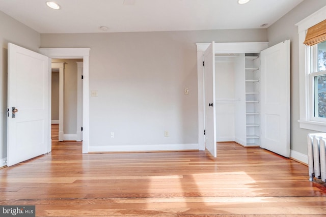 unfurnished bedroom with light hardwood / wood-style floors, radiator heating unit, and a closet