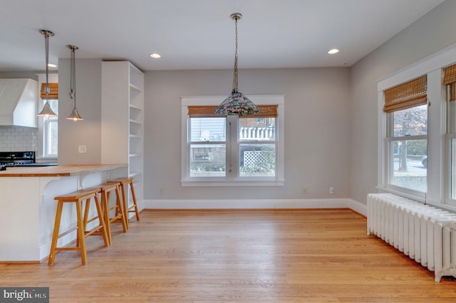 kitchen with light hardwood / wood-style floors, a kitchen bar, radiator heating unit, and pendant lighting