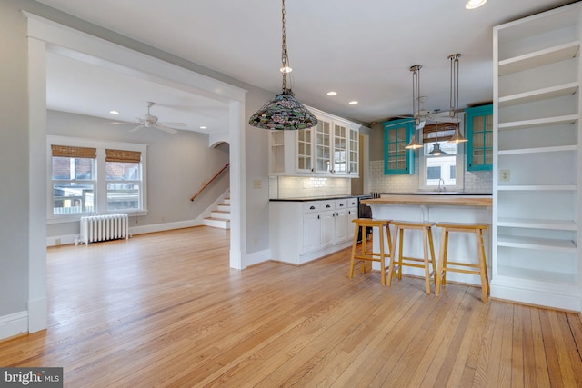 kitchen with light hardwood / wood-style floors, plenty of natural light, radiator heating unit, and white cabinetry