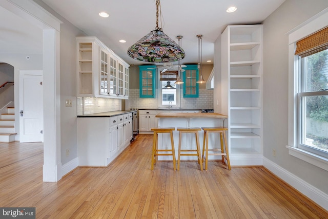 kitchen featuring light hardwood / wood-style flooring, decorative backsplash, a breakfast bar area, and white cabinets