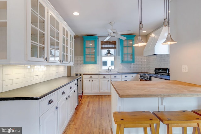 kitchen featuring a kitchen bar, white cabinets, black gas stove, custom exhaust hood, and light wood-type flooring