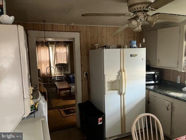 kitchen featuring ceiling fan, wooden walls, white refrigerator with ice dispenser, white refrigerator, and white cabinetry