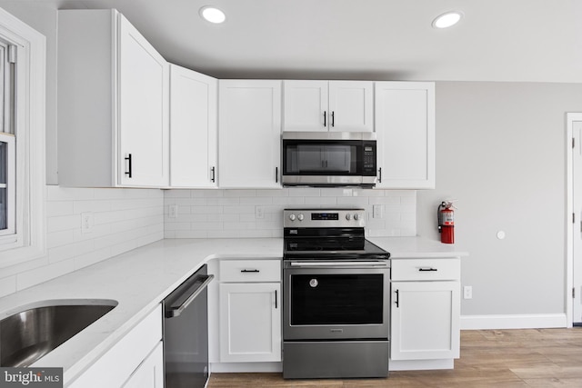 kitchen featuring decorative backsplash, appliances with stainless steel finishes, light hardwood / wood-style flooring, and white cabinetry