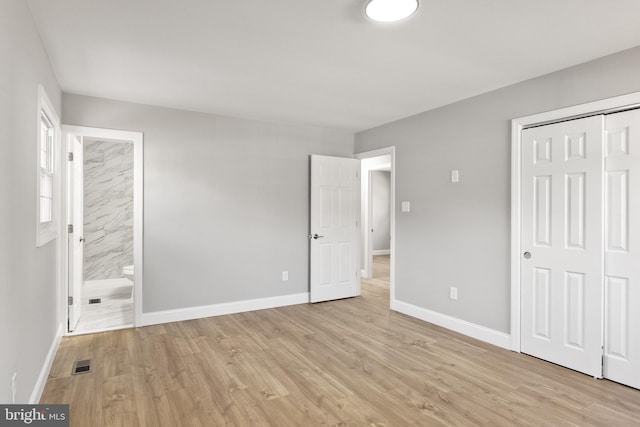 unfurnished bedroom featuring light wood-type flooring, ensuite bath, and a closet