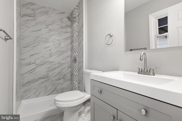 bathroom featuring a tile shower, vanity, and toilet