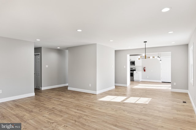 unfurnished living room featuring a chandelier and light wood-type flooring