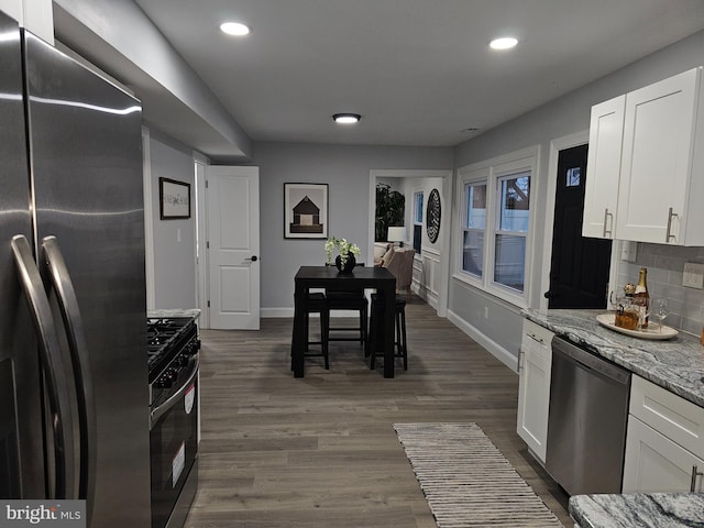 kitchen with backsplash, dark wood-type flooring, light stone counters, white cabinetry, and stainless steel appliances