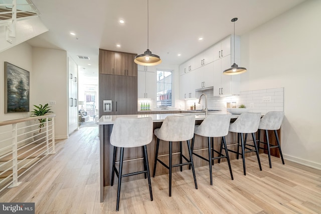 kitchen featuring a kitchen bar, white cabinets, hanging light fixtures, and light hardwood / wood-style floors