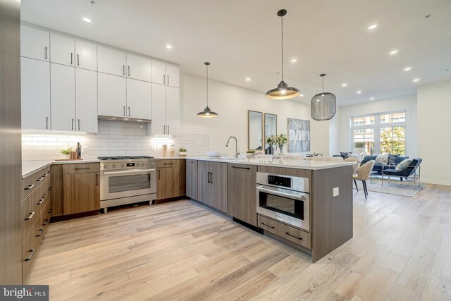 kitchen with appliances with stainless steel finishes, hanging light fixtures, white cabinets, and light hardwood / wood-style floors