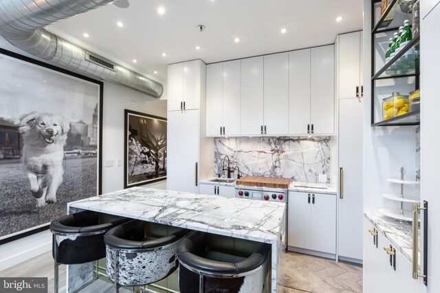 kitchen featuring decorative backsplash, a kitchen breakfast bar, sink, white cabinetry, and light stone counters