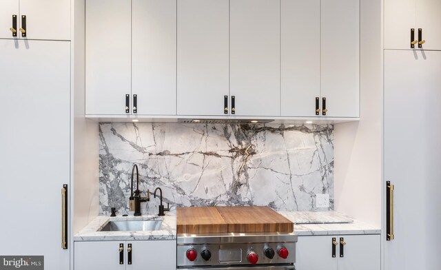 bar with light stone countertops, sink, white cabinetry, and tasteful backsplash