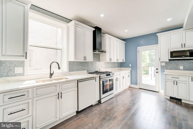 kitchen featuring decorative backsplash, stainless steel appliances, wall chimney range hood, a sink, and dark wood-type flooring