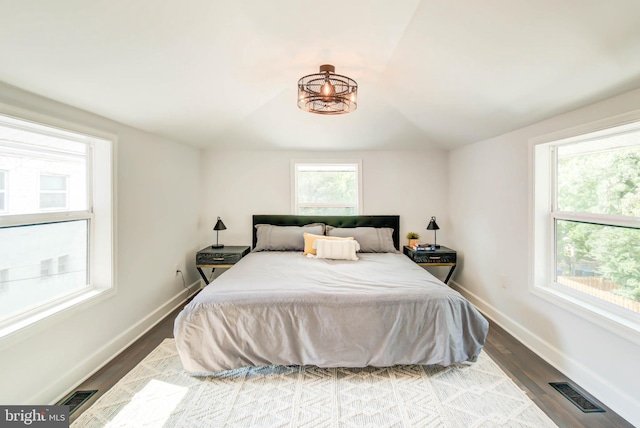 bedroom with wood finished floors, visible vents, vaulted ceiling, and baseboards