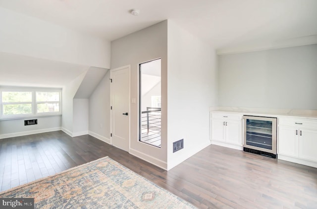 additional living space with wine cooler, vaulted ceiling, bar area, and dark hardwood / wood-style floors