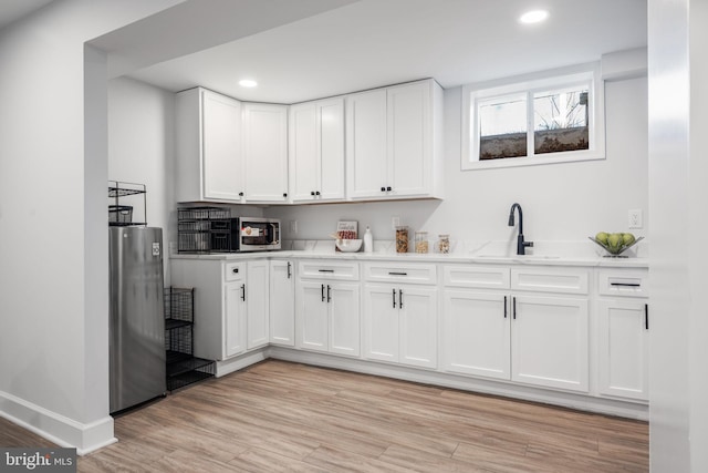bar featuring light wood-type flooring, baseboards, recessed lighting, and a sink