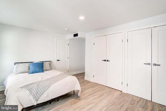bedroom featuring recessed lighting, multiple closets, visible vents, baseboards, and wood finished floors
