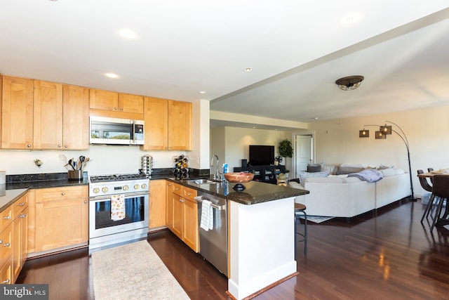 kitchen with sink, kitchen peninsula, stainless steel appliances, dark stone countertops, and dark hardwood / wood-style floors