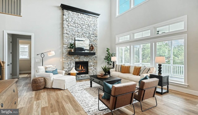 living room with light hardwood / wood-style floors, a stone fireplace, and a towering ceiling