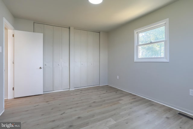 unfurnished bedroom with light hardwood / wood-style flooring and two closets