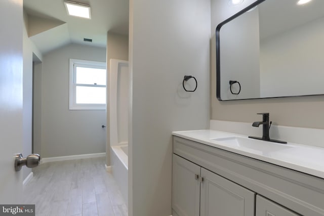 bathroom with vanity, vaulted ceiling, a bathtub, and wood-type flooring