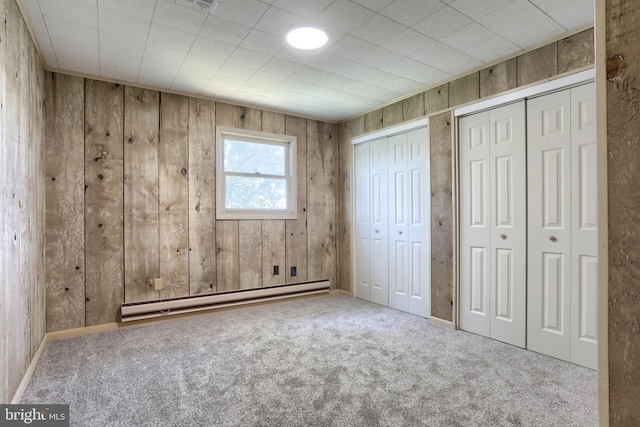 unfurnished bedroom featuring baseboard heating, multiple closets, wooden walls, and carpet