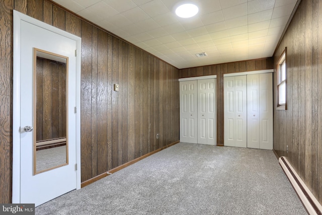 unfurnished bedroom featuring wood walls, carpet floors, two closets, and a baseboard radiator