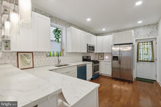 kitchen with kitchen peninsula, light stone counters, appliances with stainless steel finishes, white cabinetry, and sink