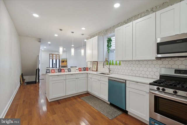 kitchen featuring kitchen peninsula, hanging light fixtures, appliances with stainless steel finishes, white cabinetry, and sink