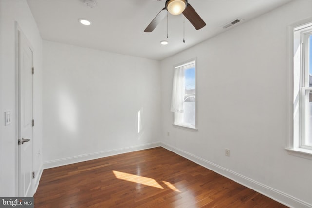 empty room with a wealth of natural light, dark wood-type flooring, and ceiling fan