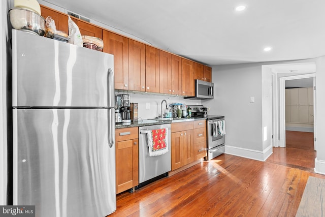 kitchen featuring dark hardwood / wood-style floors, sink, stainless steel appliances, and dark stone counters