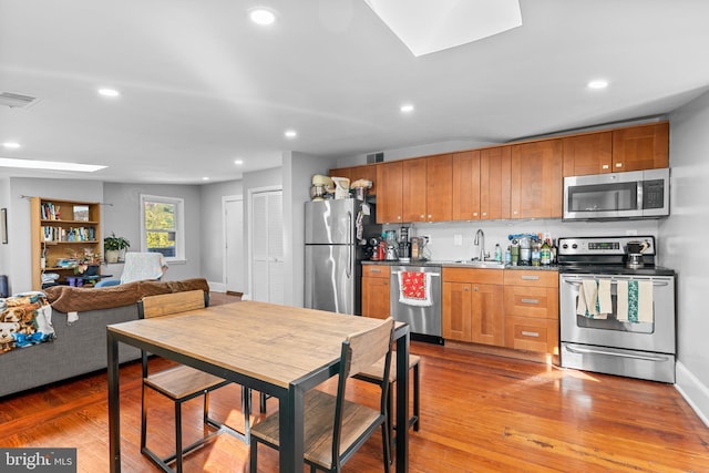 kitchen featuring sink, light wood-type flooring, stainless steel appliances, and a skylight