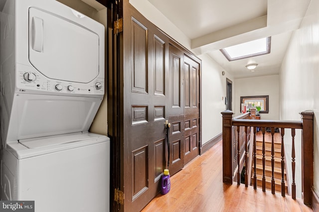 clothes washing area featuring stacked washer and dryer, a skylight, and light hardwood / wood-style floors