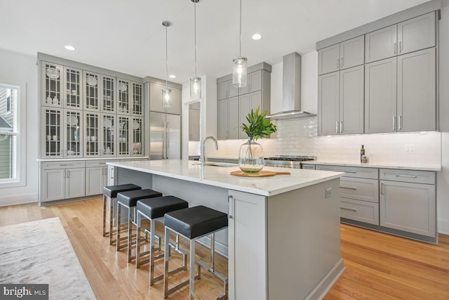 kitchen featuring a kitchen bar, light wood-type flooring, wall chimney exhaust hood, gray cabinets, and a center island with sink