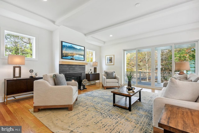 living room featuring a tiled fireplace, beamed ceiling, and light wood-type flooring