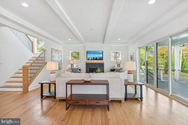 living room featuring light hardwood / wood-style floors, beamed ceiling, and a tile fireplace