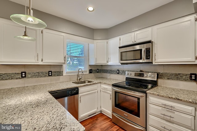 kitchen with appliances with stainless steel finishes, white cabinets, sink, and hanging light fixtures