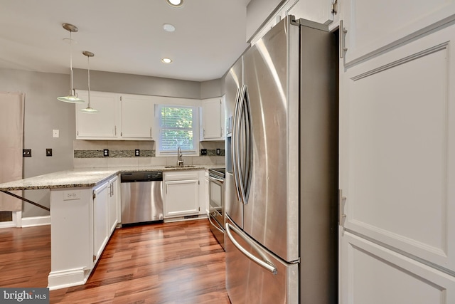 kitchen featuring kitchen peninsula, stainless steel appliances, pendant lighting, light wood-type flooring, and white cabinets