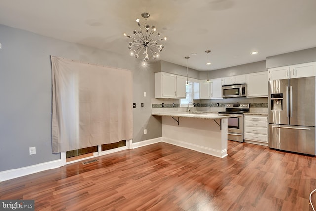 kitchen featuring appliances with stainless steel finishes, light wood-type flooring, kitchen peninsula, white cabinetry, and a notable chandelier