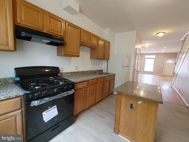 kitchen with black gas range, light wood-type flooring, a center island, sink, and light stone counters