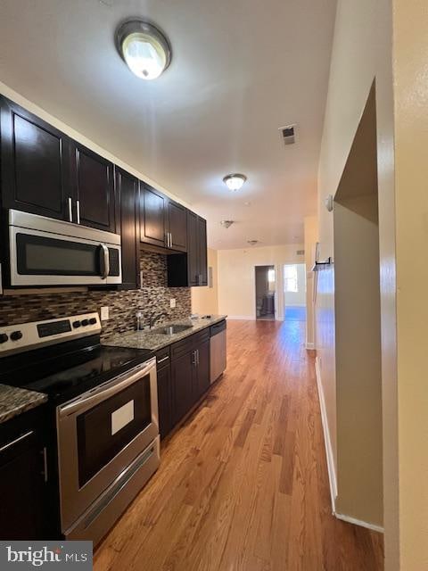 kitchen with sink, light hardwood / wood-style floors, stainless steel appliances, and backsplash