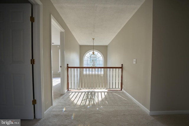 corridor featuring carpet, a textured ceiling, and an inviting chandelier