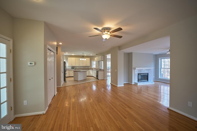 unfurnished living room featuring a tiled fireplace, ceiling fan, and light hardwood / wood-style floors