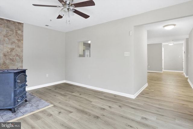 unfurnished living room with ceiling fan, a wood stove, and light wood-type flooring