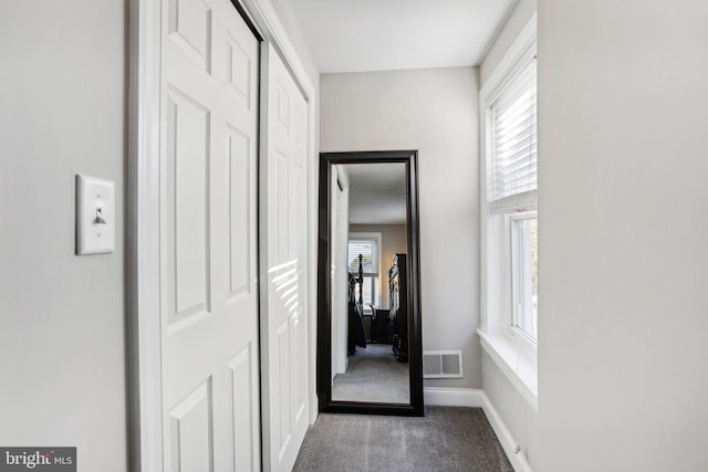 hallway featuring dark colored carpet and a wealth of natural light