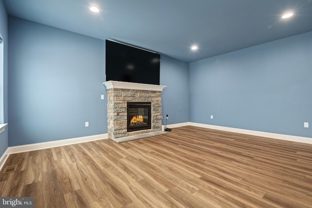 unfurnished living room featuring wood-type flooring and a stone fireplace