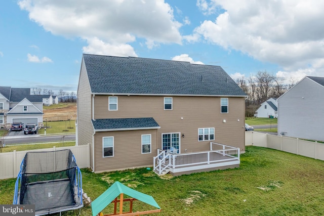 back of house featuring a lawn, a wooden deck, and a trampoline